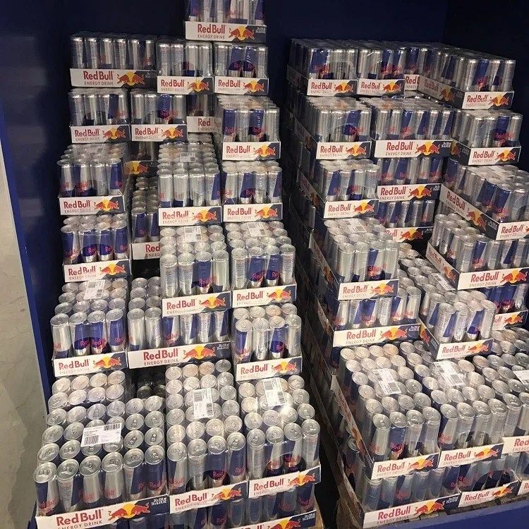 Display of many Red Bull energy drink cases stacked in a store, silver and blue cans visible.