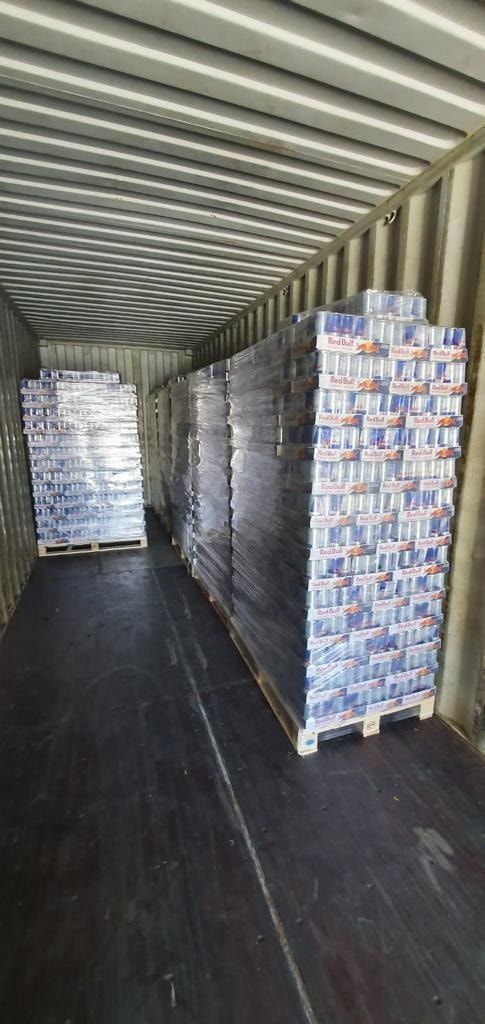 Inside a cargo container, stacked pallets of canned beverages.