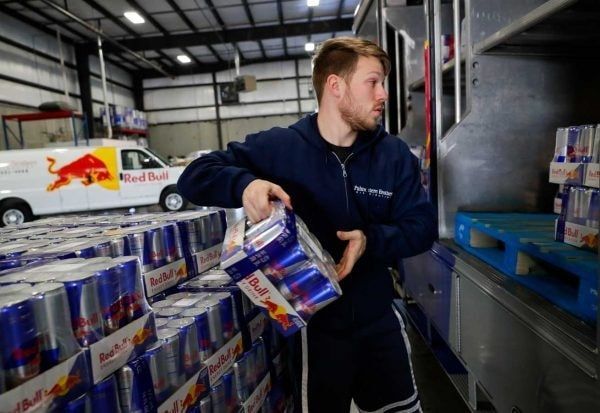 Man in blue uniform loads Red Bull cans in a warehouse with a Red Bull van.