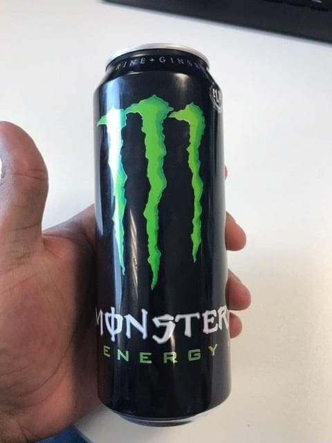 Hand holding a black Monster Energy drink can with a green claw logo.