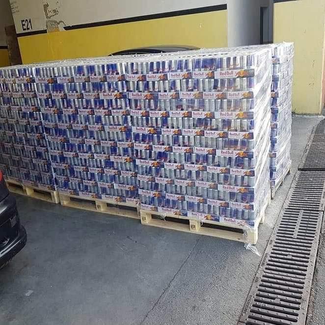 Pallets stacked with many cases of Red Bull energy drinks, wrapped in plastic.