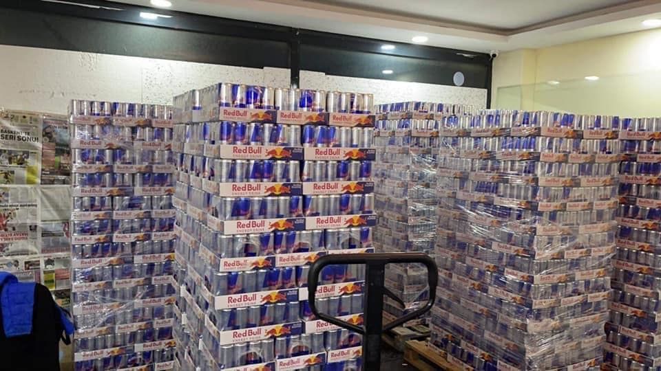Stacks of Red Bull cases wrapped in plastic, inside a warehouse.