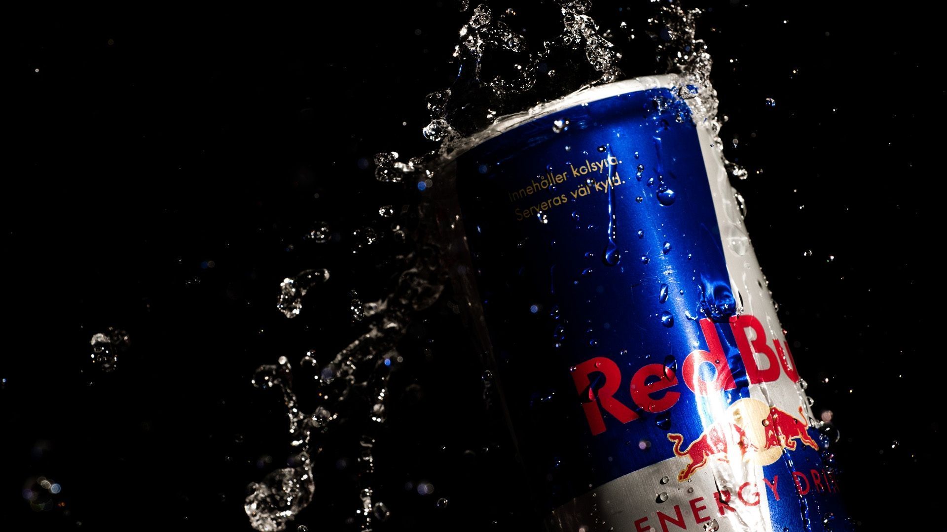 Red Bull can with blue and red branding, splashing water against a black background.
