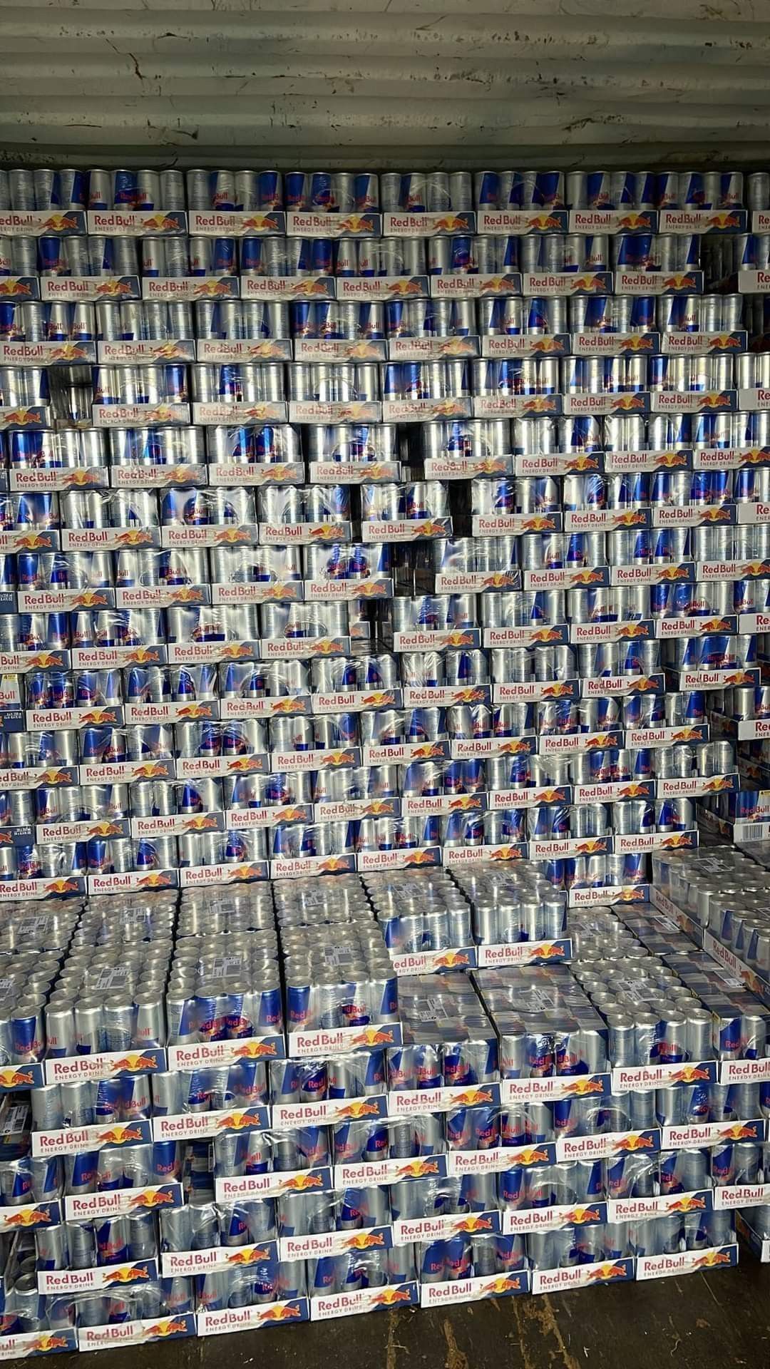Stacks of Red Bull cans and packs fill a container, mostly blue, silver, and white.