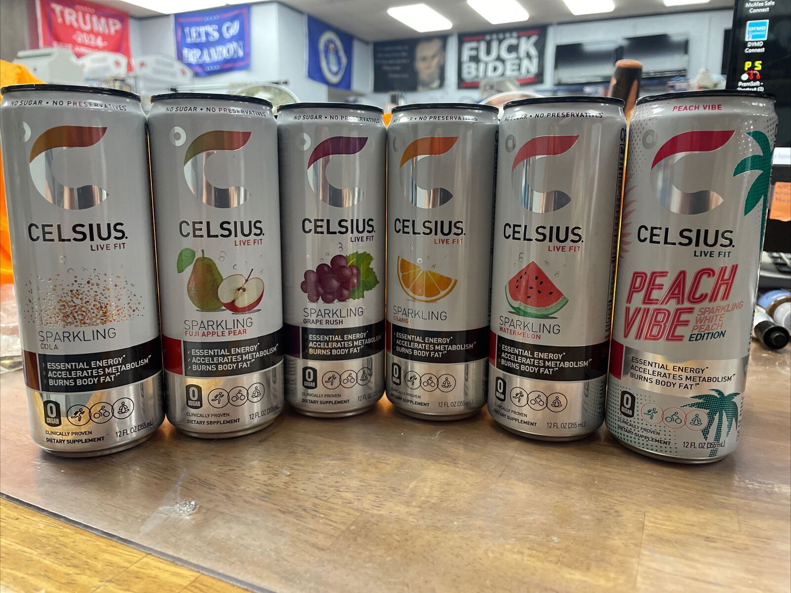 Six Celsius energy drink cans, flavors include sparkling cola, pear, grape, orange, watermelon, and peach.