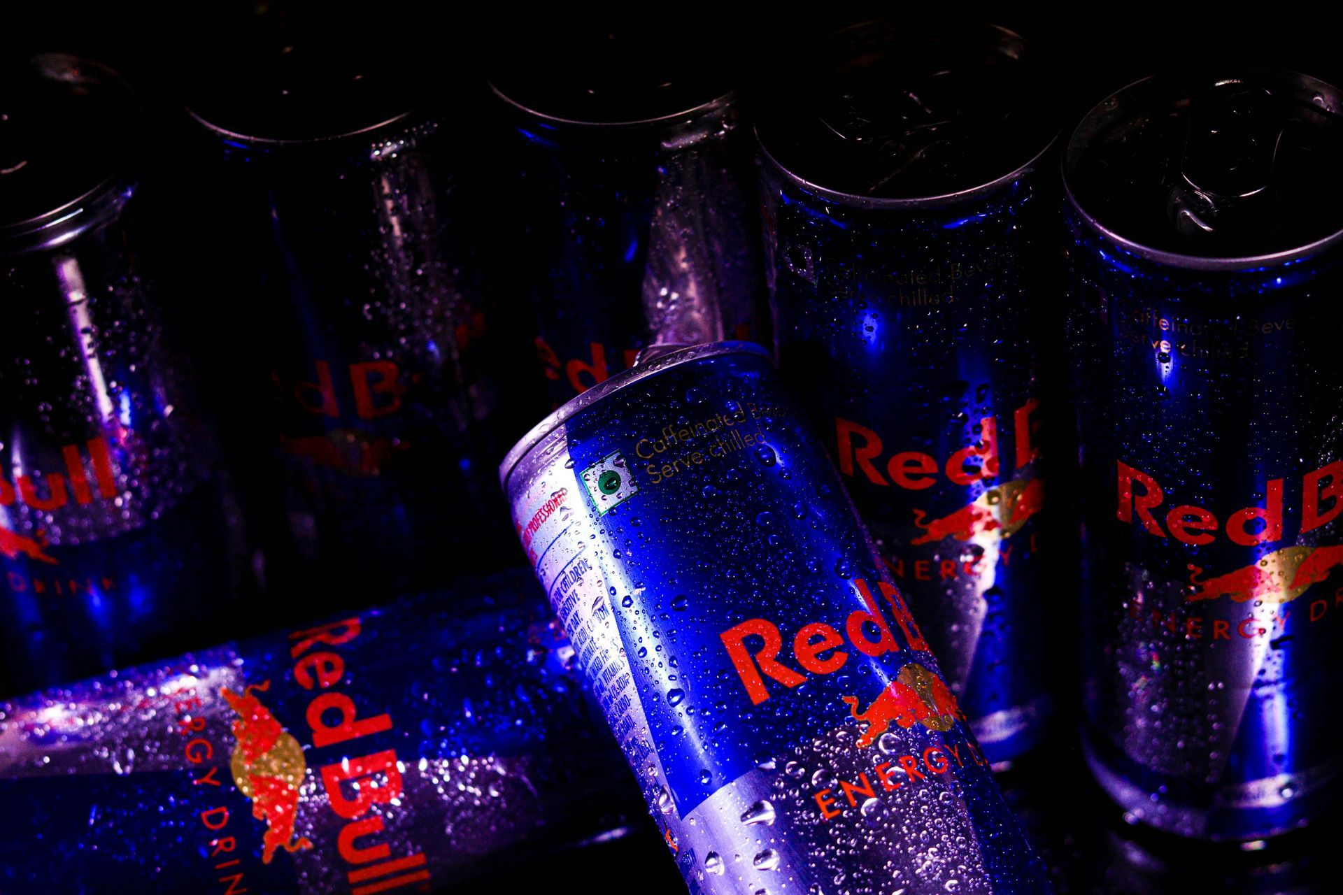 Close-up of several chilled Red Bull cans; blue and silver with condensation and the Red Bull logo visible.
