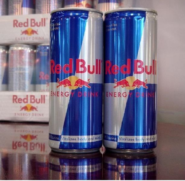 Two Red Bull energy drink cans with a display of other cans in the background.