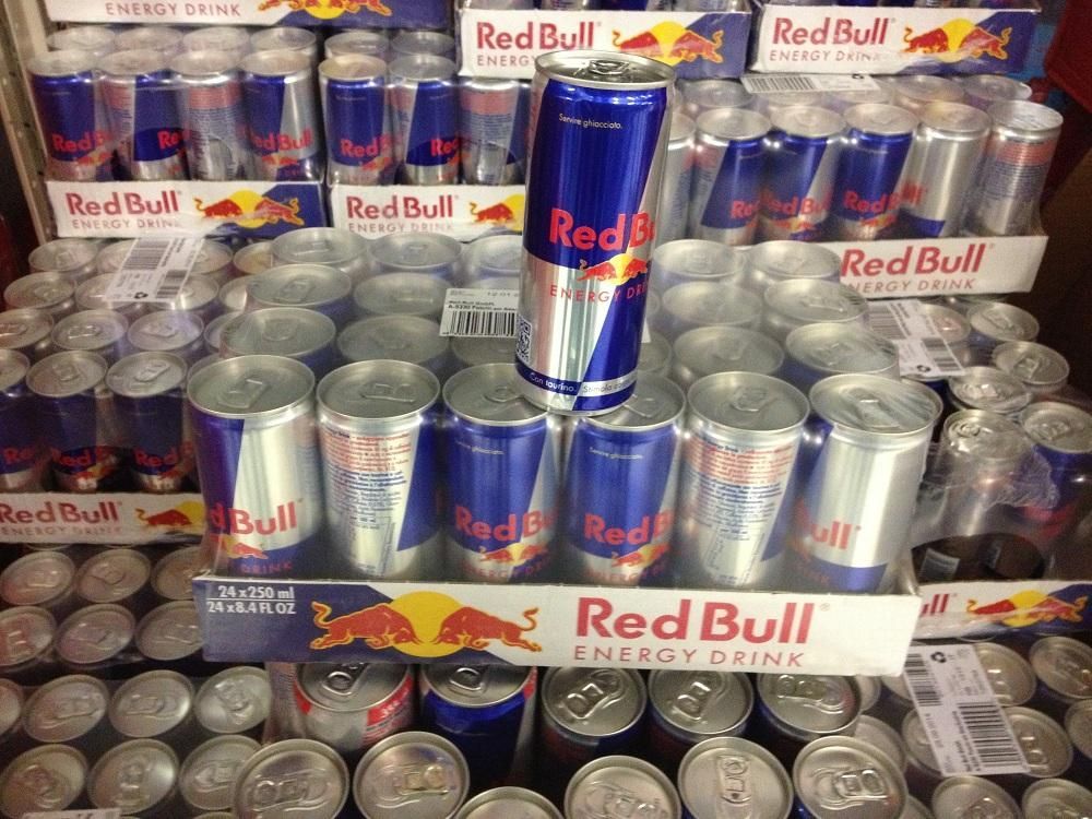 Red Bull energy drink cans stacked in cardboard trays at a store, ready for sale.