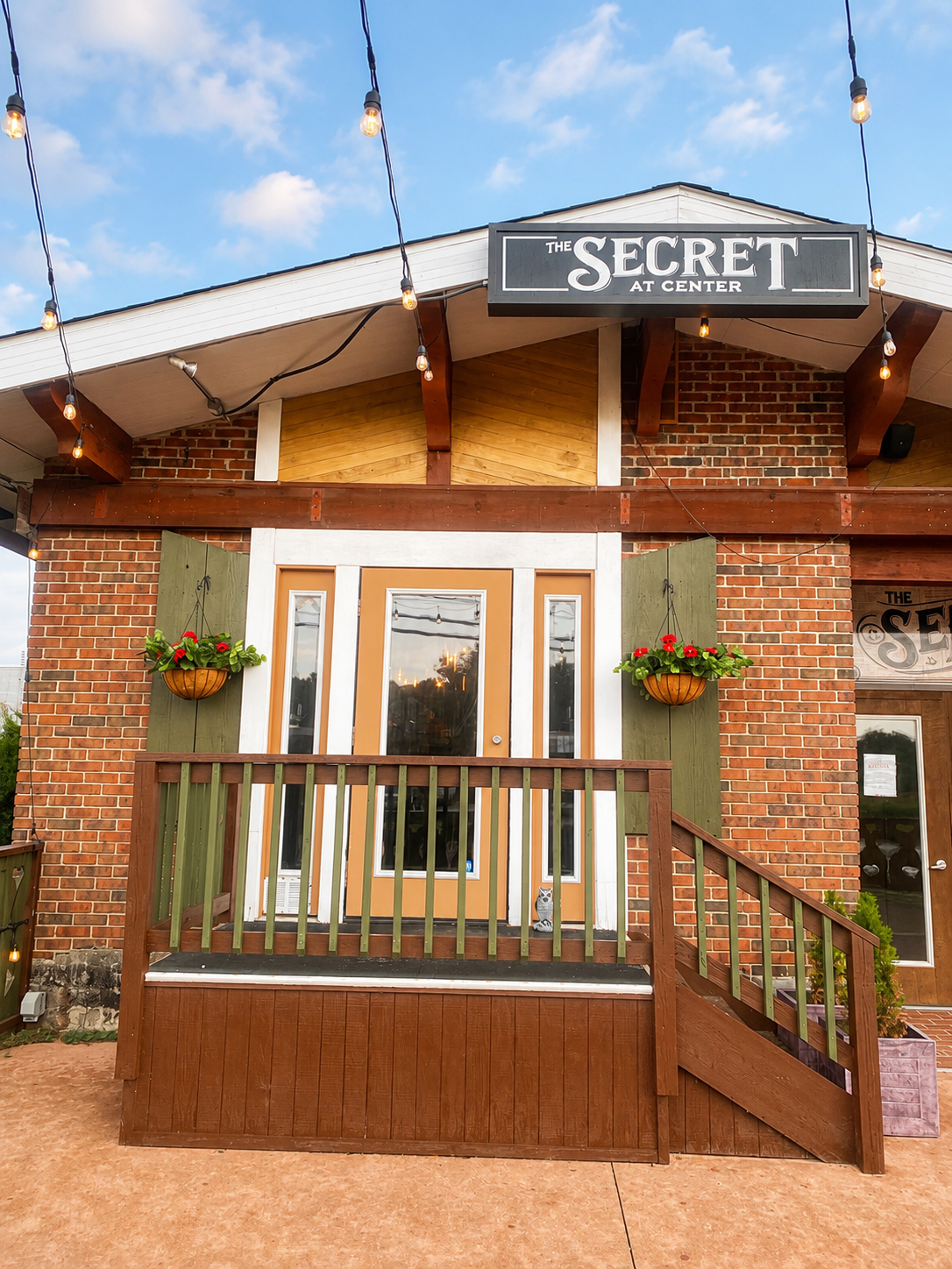 Front entrance of Secret Garden with brick facade, wooden railing, and hanging string lights