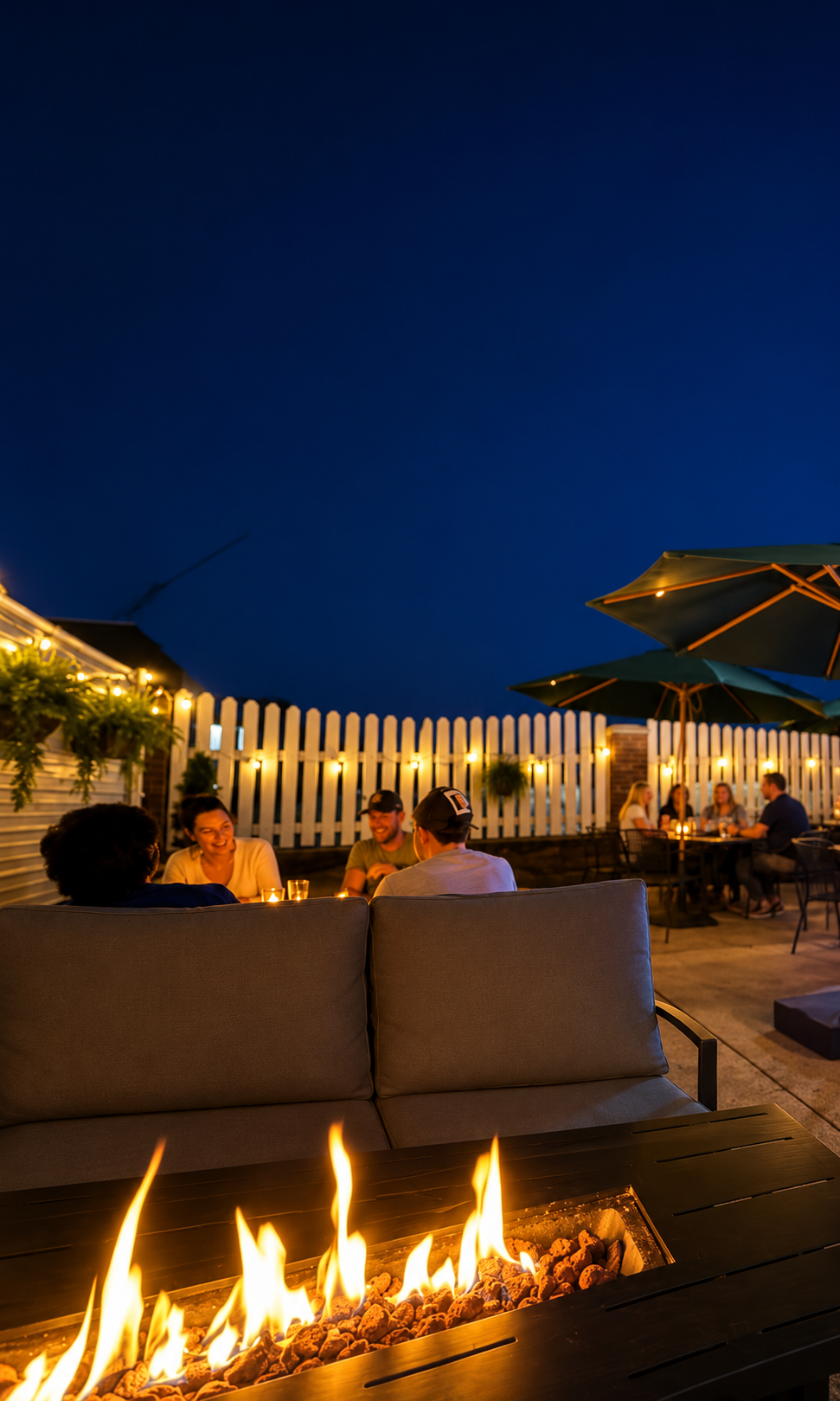 Outdoor rooftop lounge at dusk with people seated by a fire pit under a deep blue sky