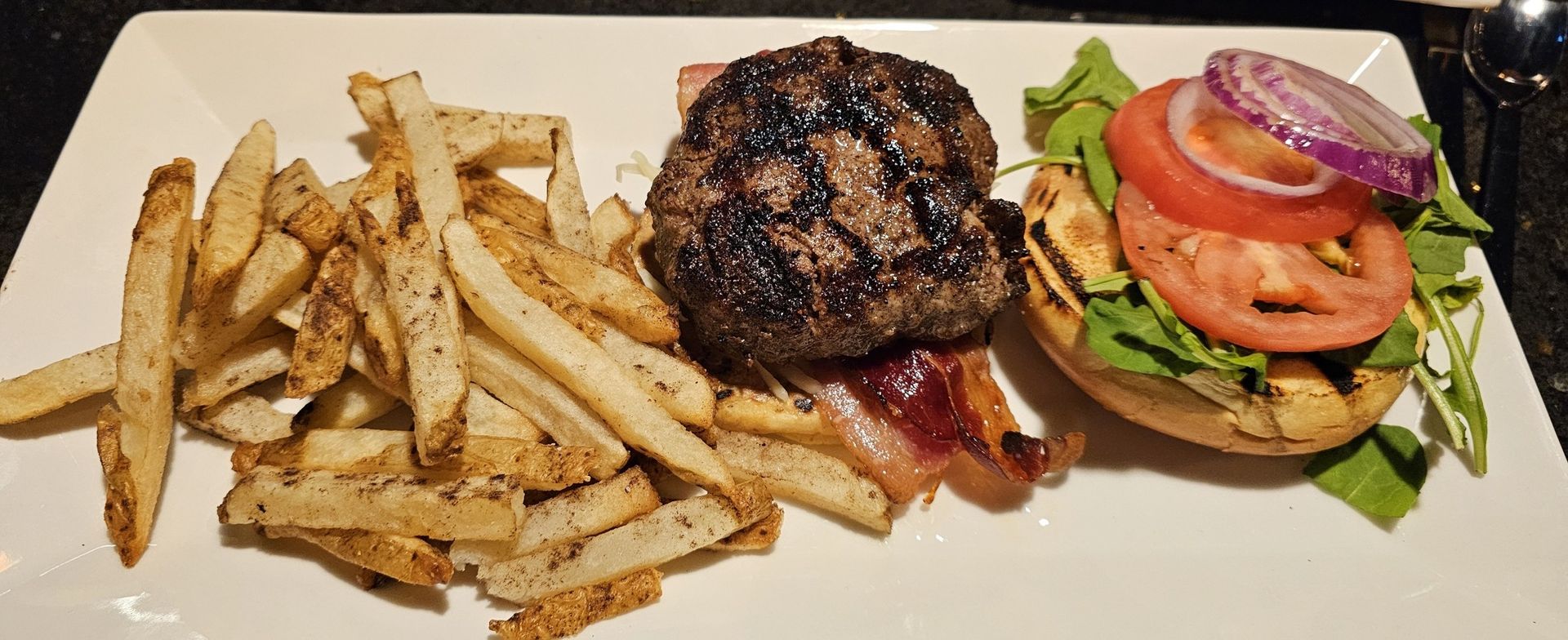 Burger with fries on a white plate. Includes a bun, lettuce, tomato, red onion, bacon, and a grilled patty. Burger with fries on a white plate. Includes a bun, lettuce, tomato, red onion, bacon, and a grilled patty.