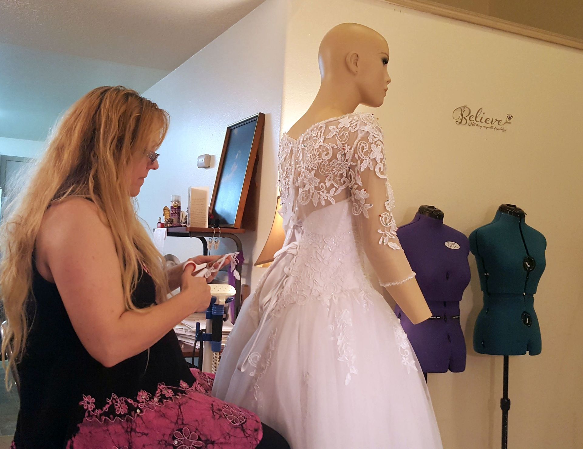 Woman fitting a white wedding dress on a mannequin. Other dress forms in the background.