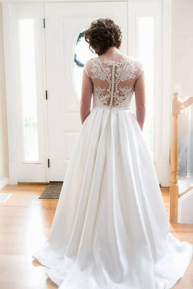 Bride in white dress with lace back, standing in a bright doorway.
