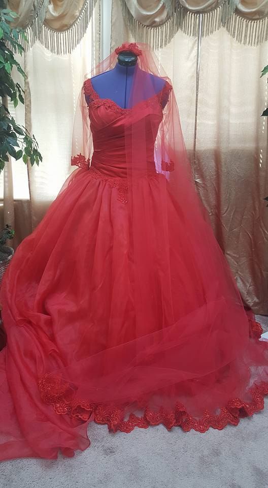Red bridal gown with a long train on a mannequin. A red veil and floral headpiece are displayed.
