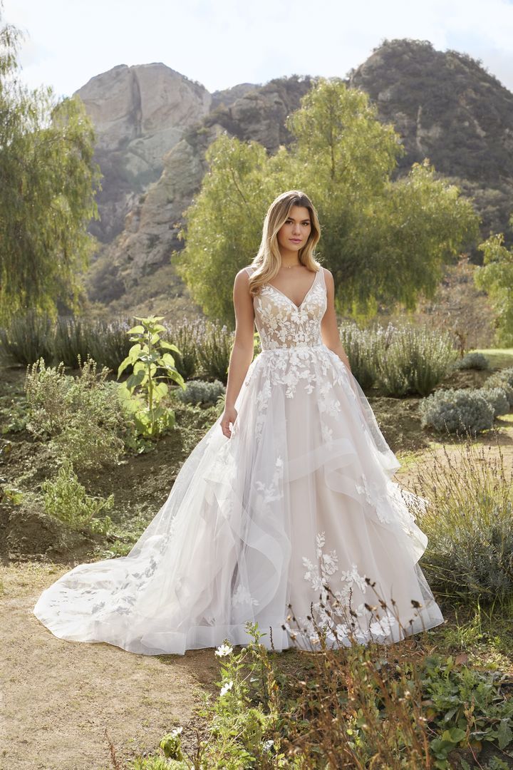 Woman in a white ballgown, long sleeves, and a tiara. She is smiling, arms crossed in front.