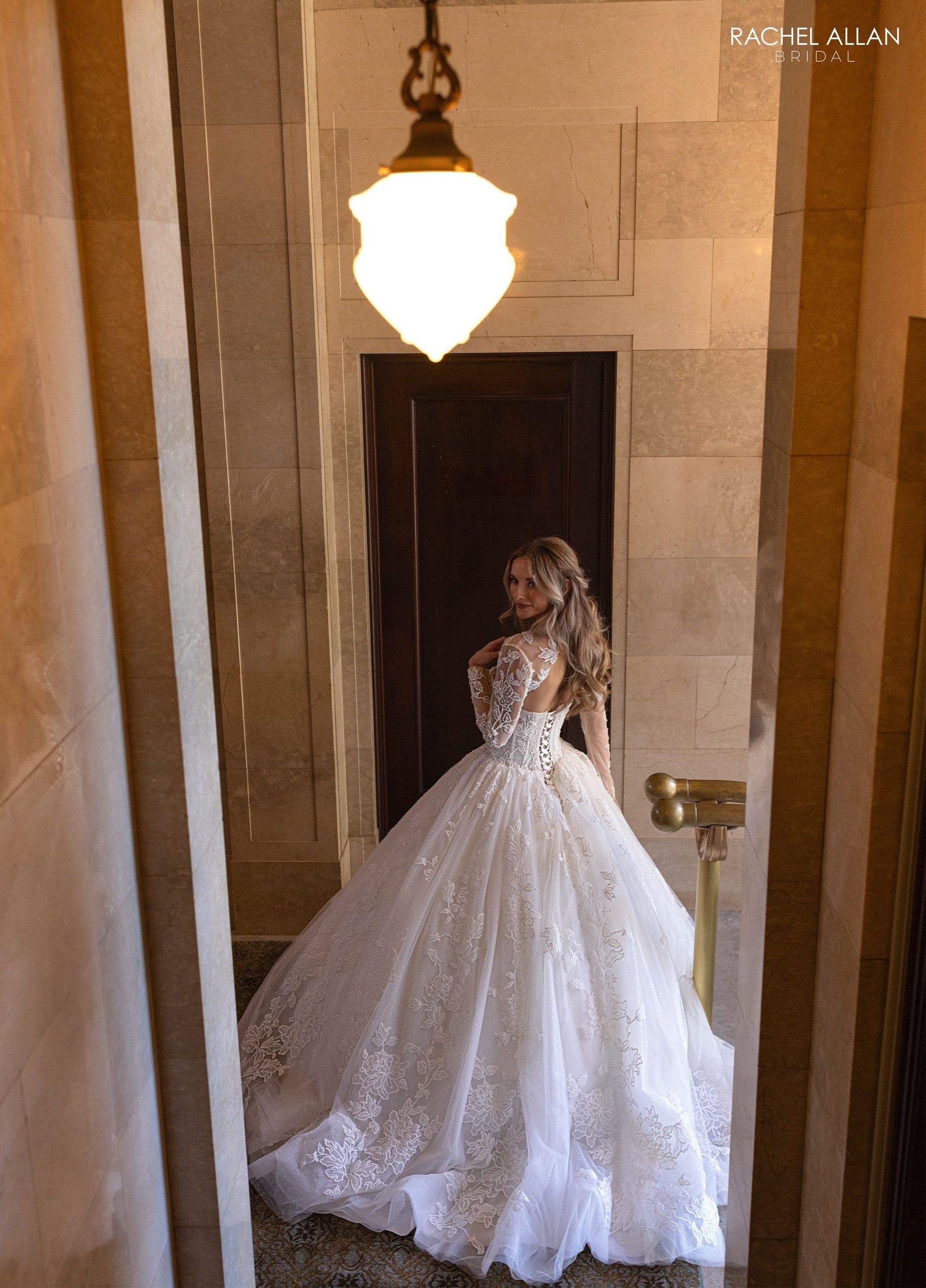Woman in white wedding dress with long sleeves, standing near doorway.
