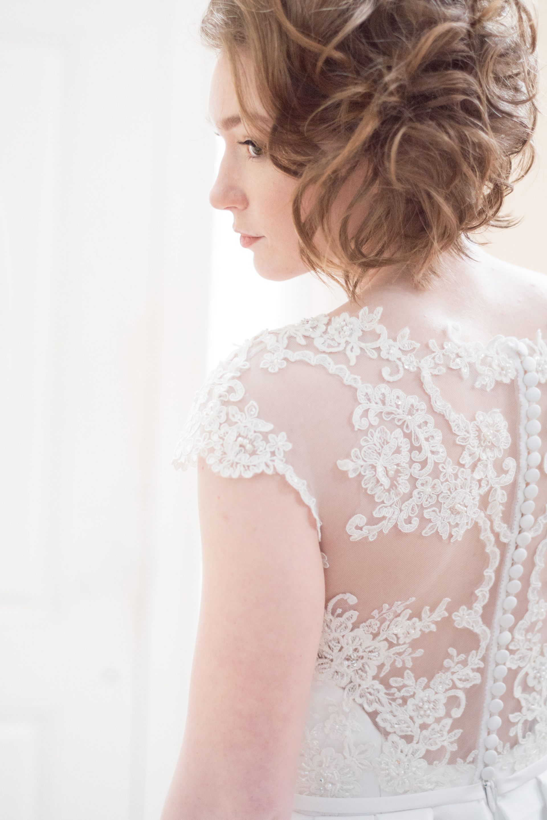 Wedding dress on a mannequin in a well-lit room with a mirror, plants, and antique furniture.