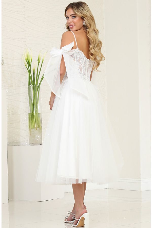 Woman in white formal dress with tulle skirt and shoulder bows, smiling.