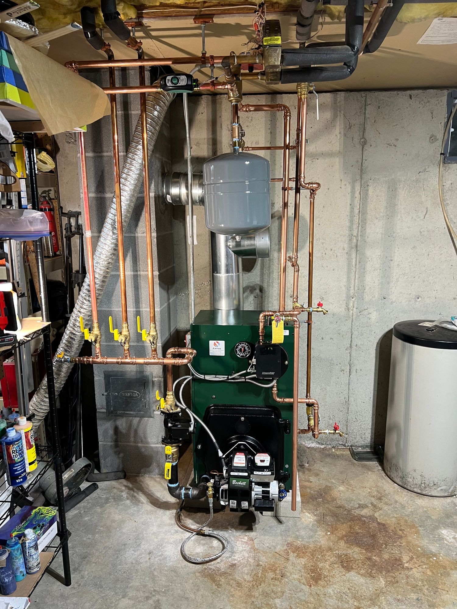 a green boiler is sitting in a basement with copper pipes .