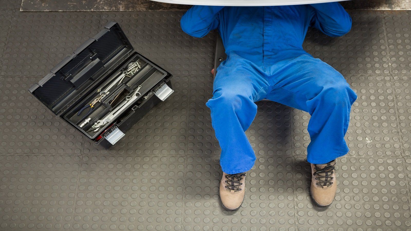 Meccanico lavorando sotto l'automobile, cassetta degli attrezzi al suo fianco