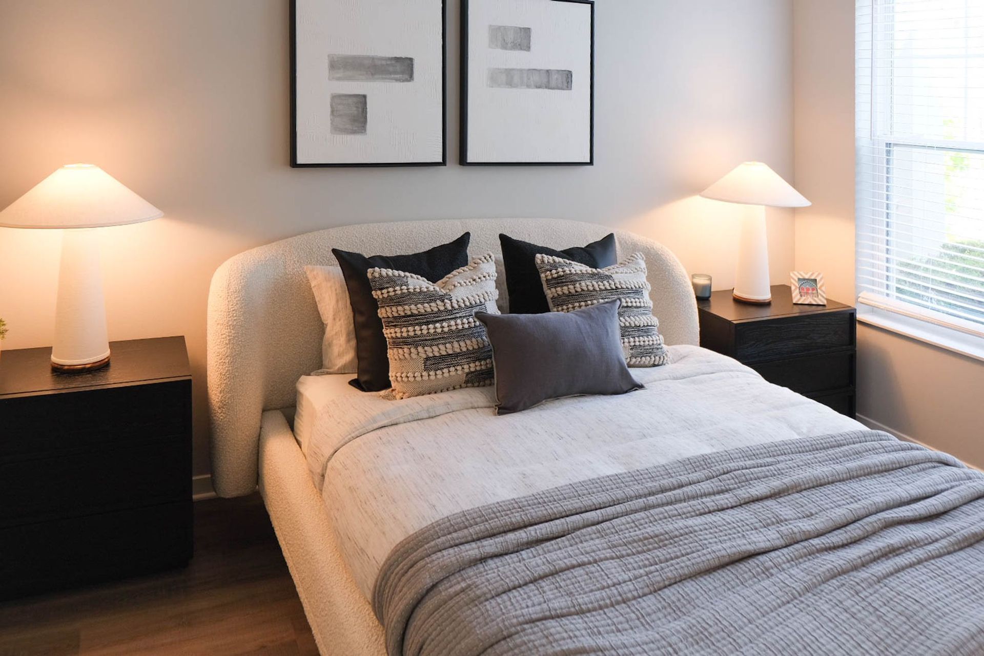 A bedroom with a bed , two nightstands , two lamps and two paintings on the wall.