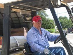 Man driving a forklift outdoors, wearing a red cap and blue shirt.