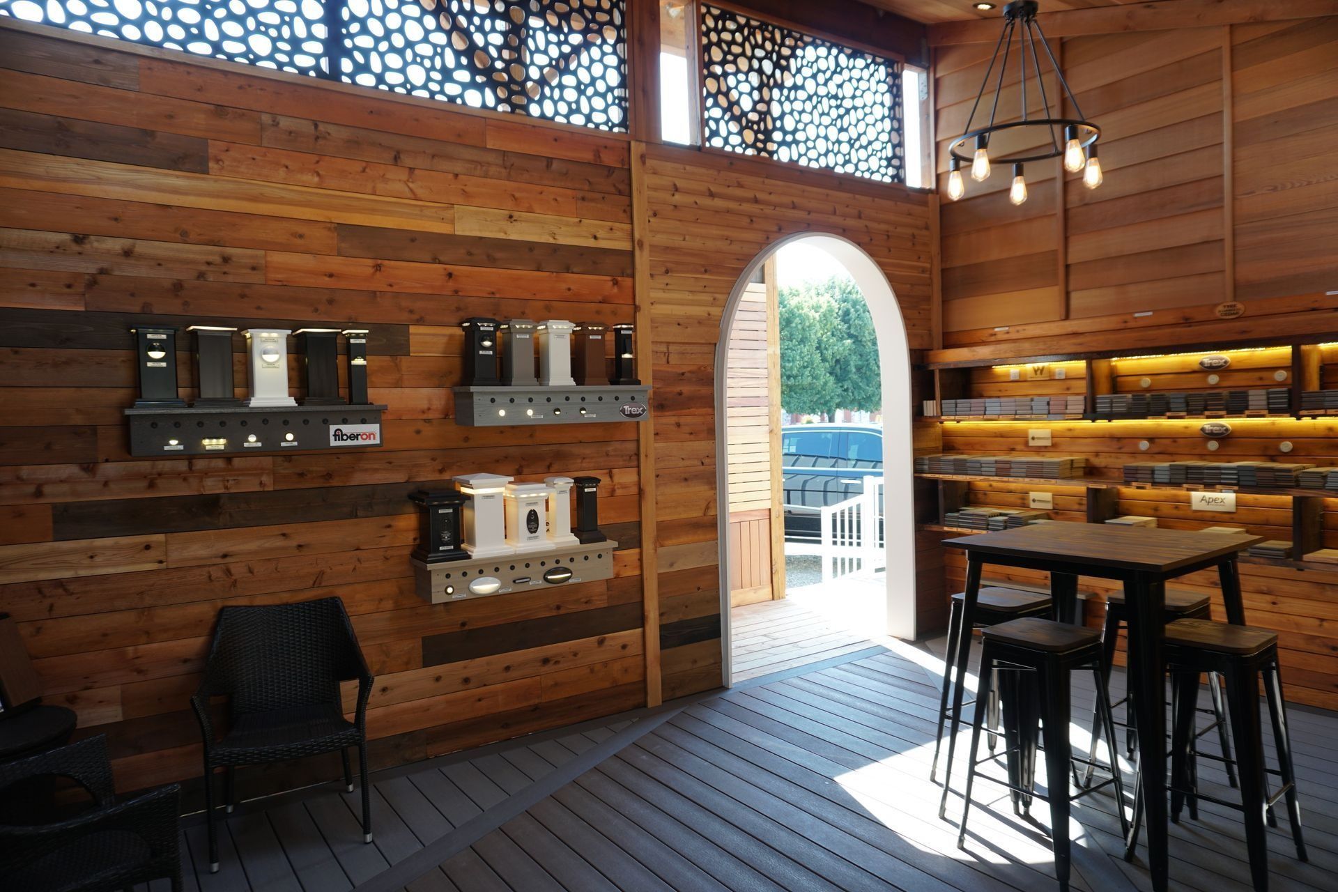 Interior of a shop with wood paneling, displays of speakers, tables, and an open doorway to an outside area.