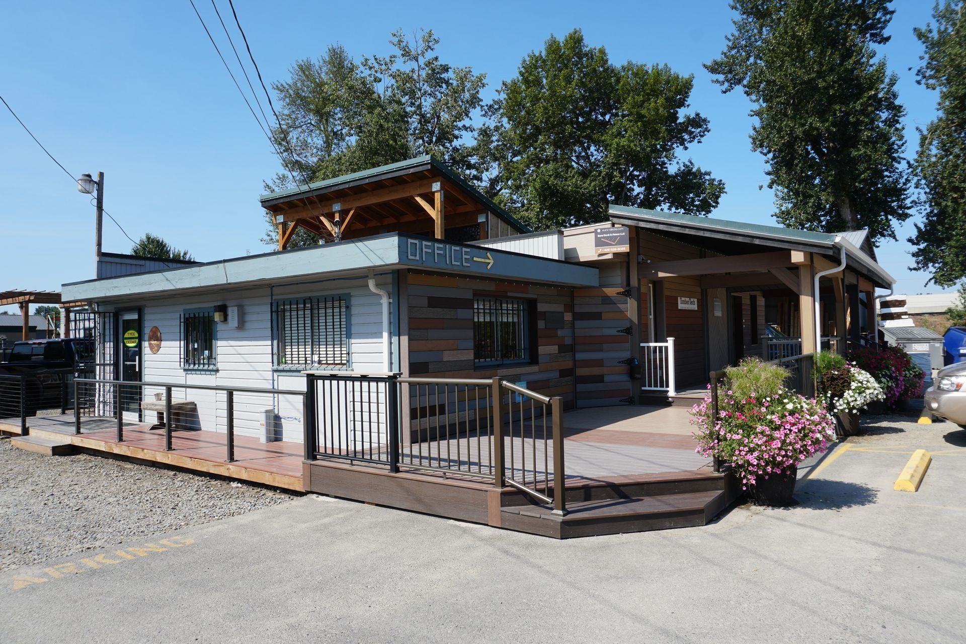 Restaurant exterior with wooden deck, brick patio, and floral planters, under a blue sky.