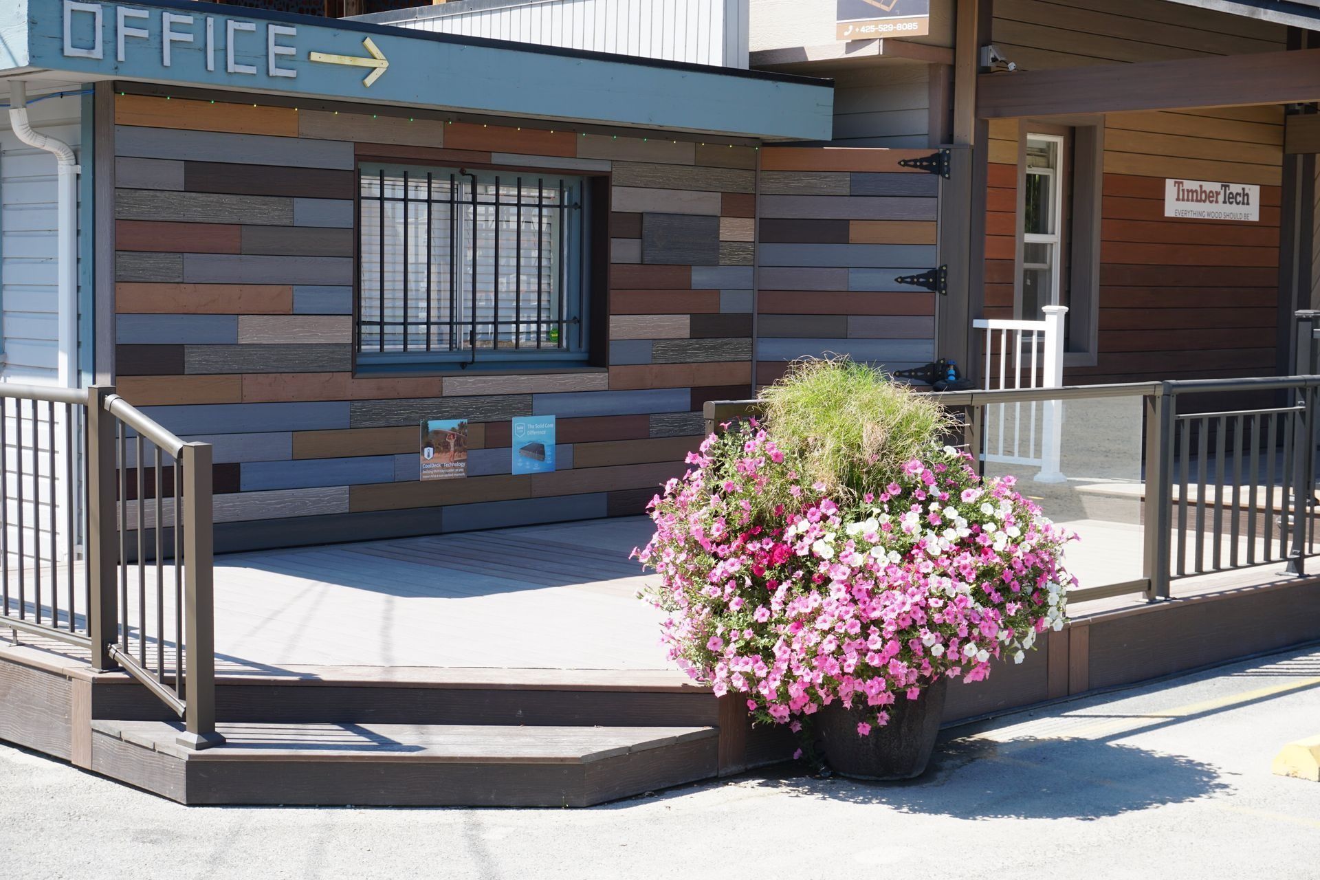 Office entrance with brown siding, a small deck, railings, and large flower pots.