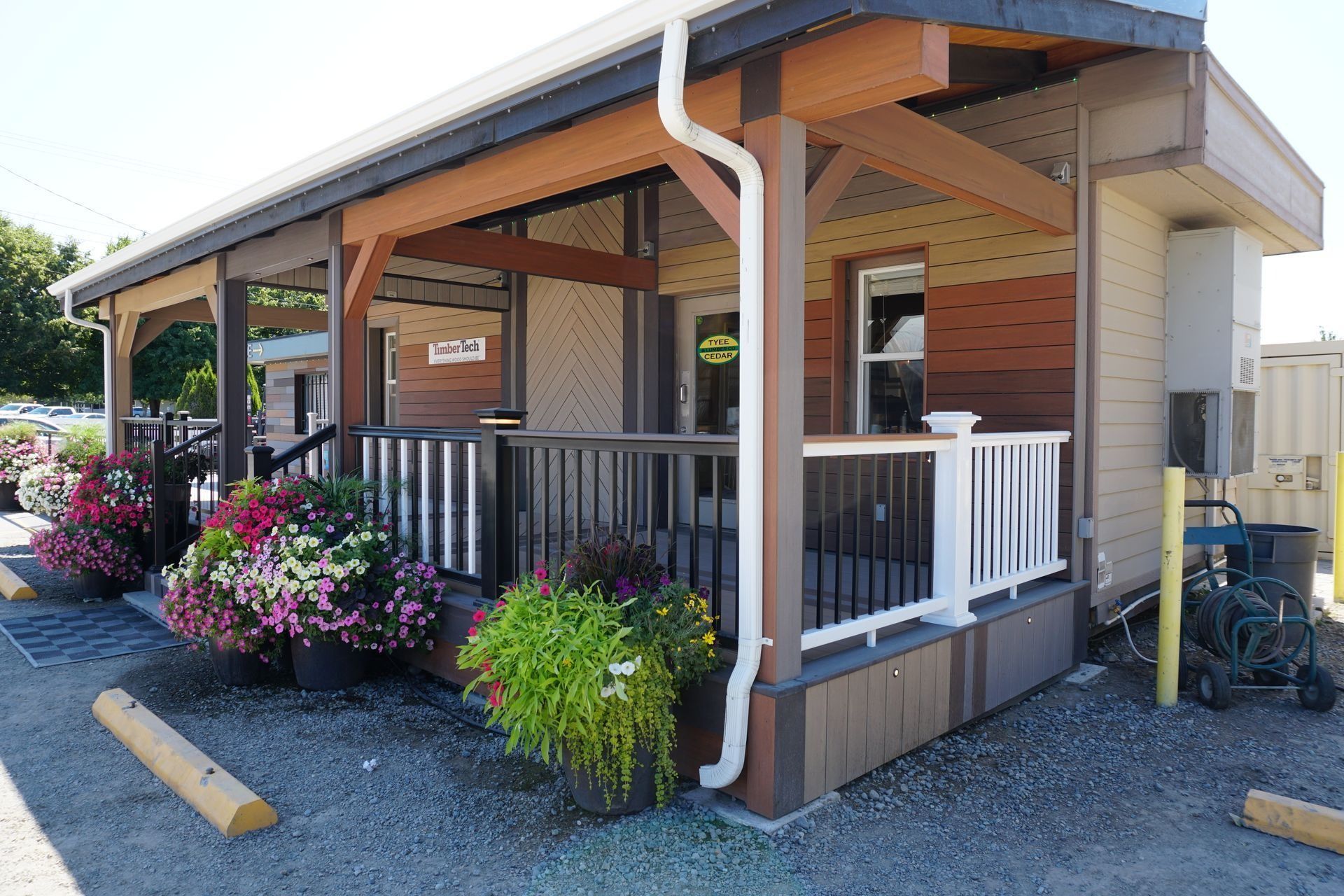 Storefront with porch, colorful flowers, brown and white railings, gutter, blue sky.