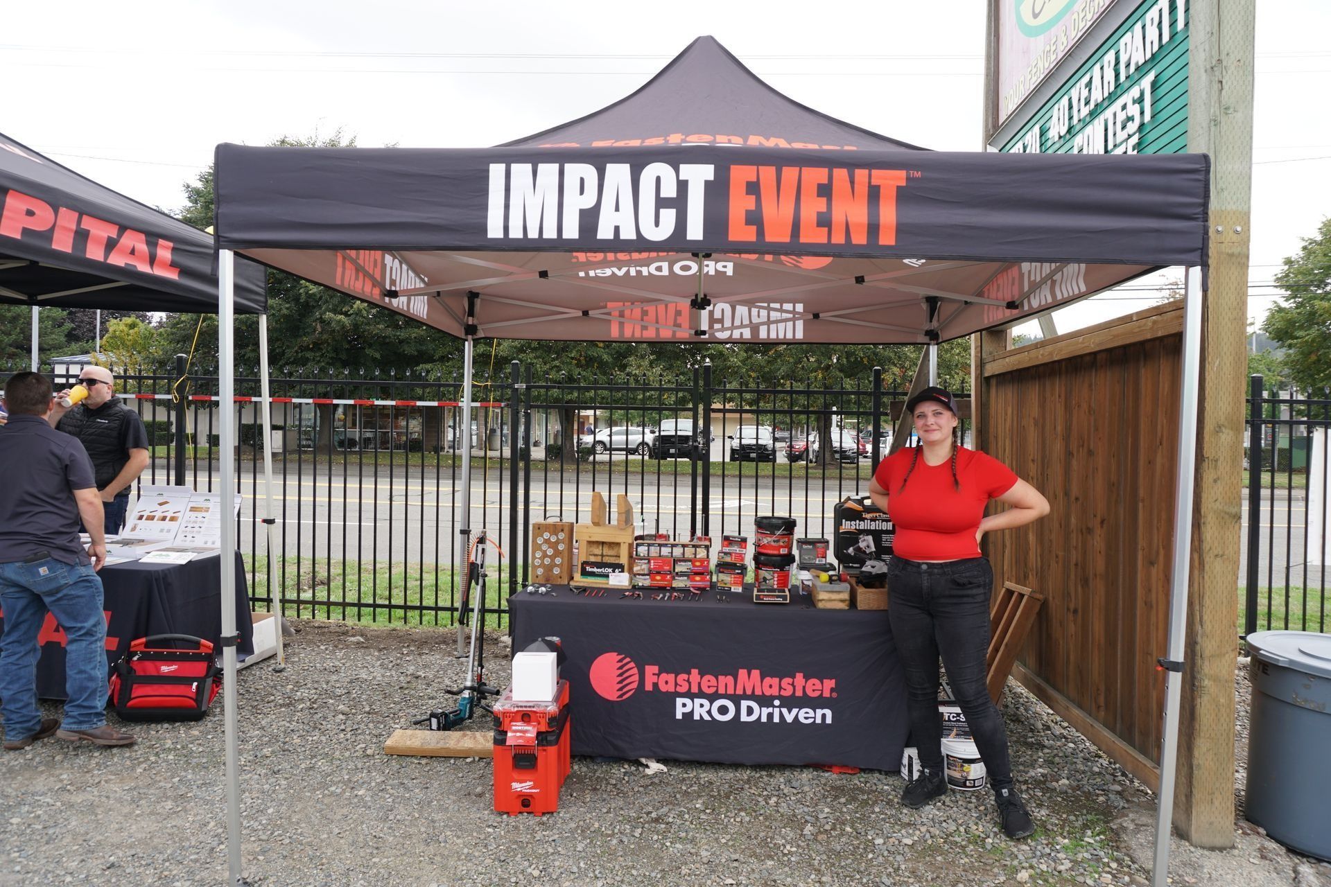 Impact Event booth with FastenMaster products, woman in red shirt poses, tools displayed.