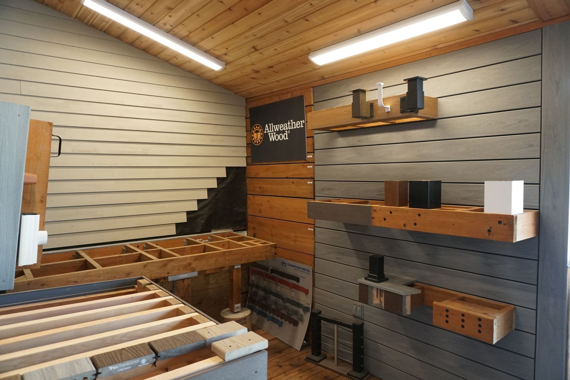 Showroom with wood and composite decking samples displayed on walls and shelving, with wood-paneled ceiling.
