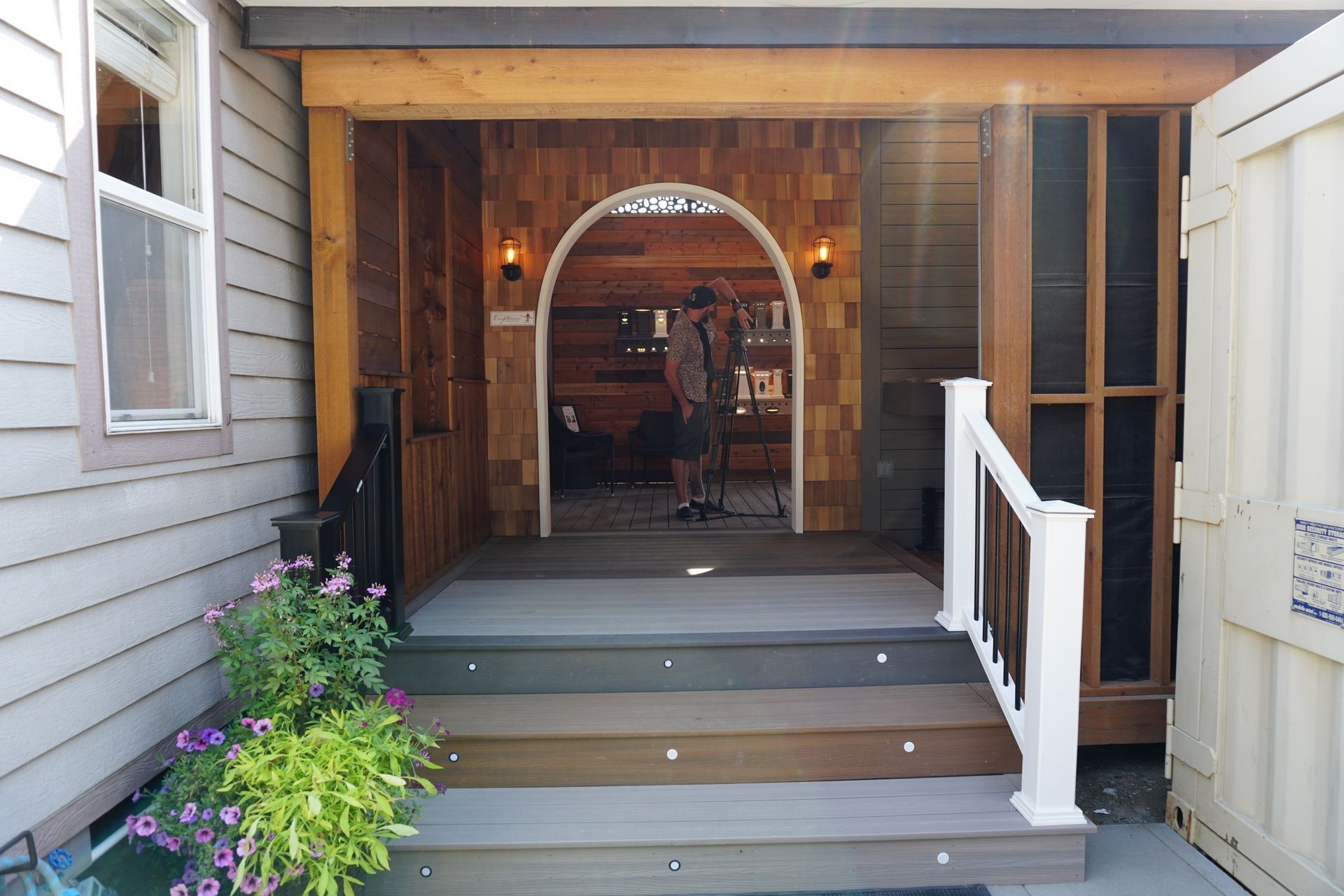 Wooden entryway with steps, arch, and person inside. White and brown tones.
