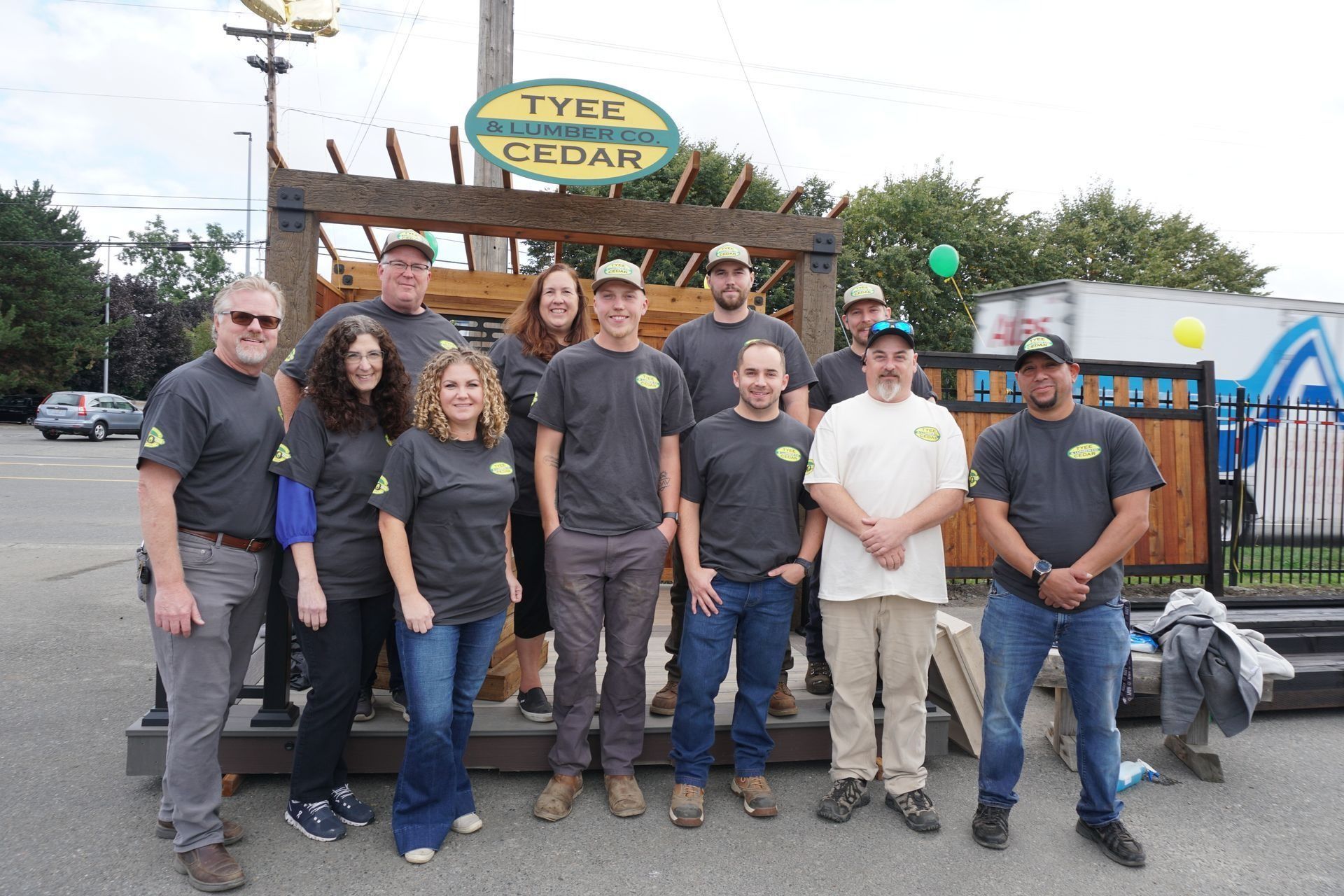 Group of people pose in front of a Type Cedar sign. All wear matching shirts and hats. Outdoor setting.