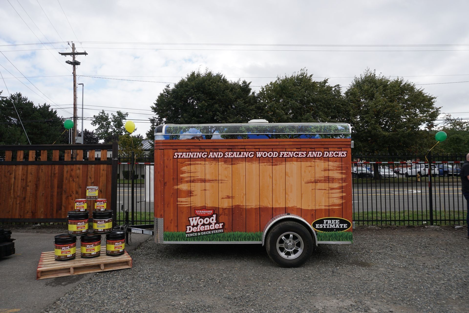 Wooden food cart with painted sign, parked on gravel. Jars of product on a pallet nearby.