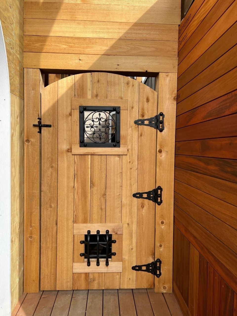 Wooden gate with two barred windows and black hinges, set into a wooden frame.