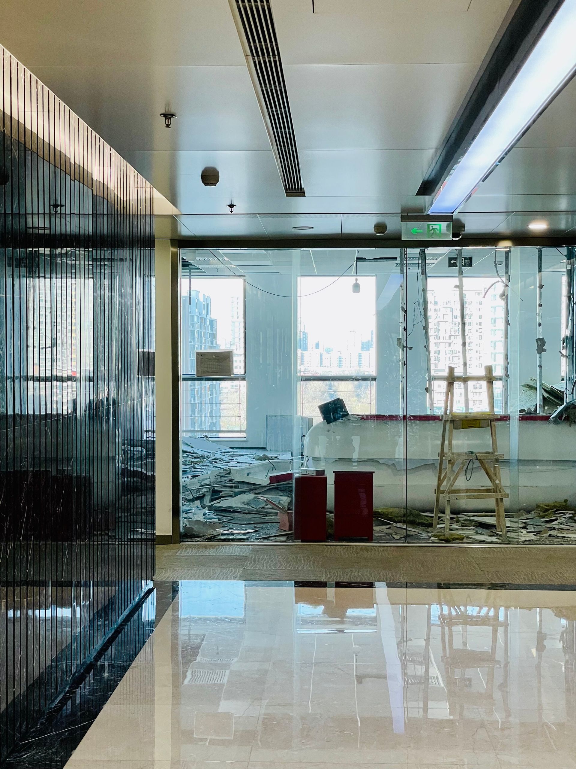Modern office hallway with glass walls, reflective floor, and construction debris near bright windows