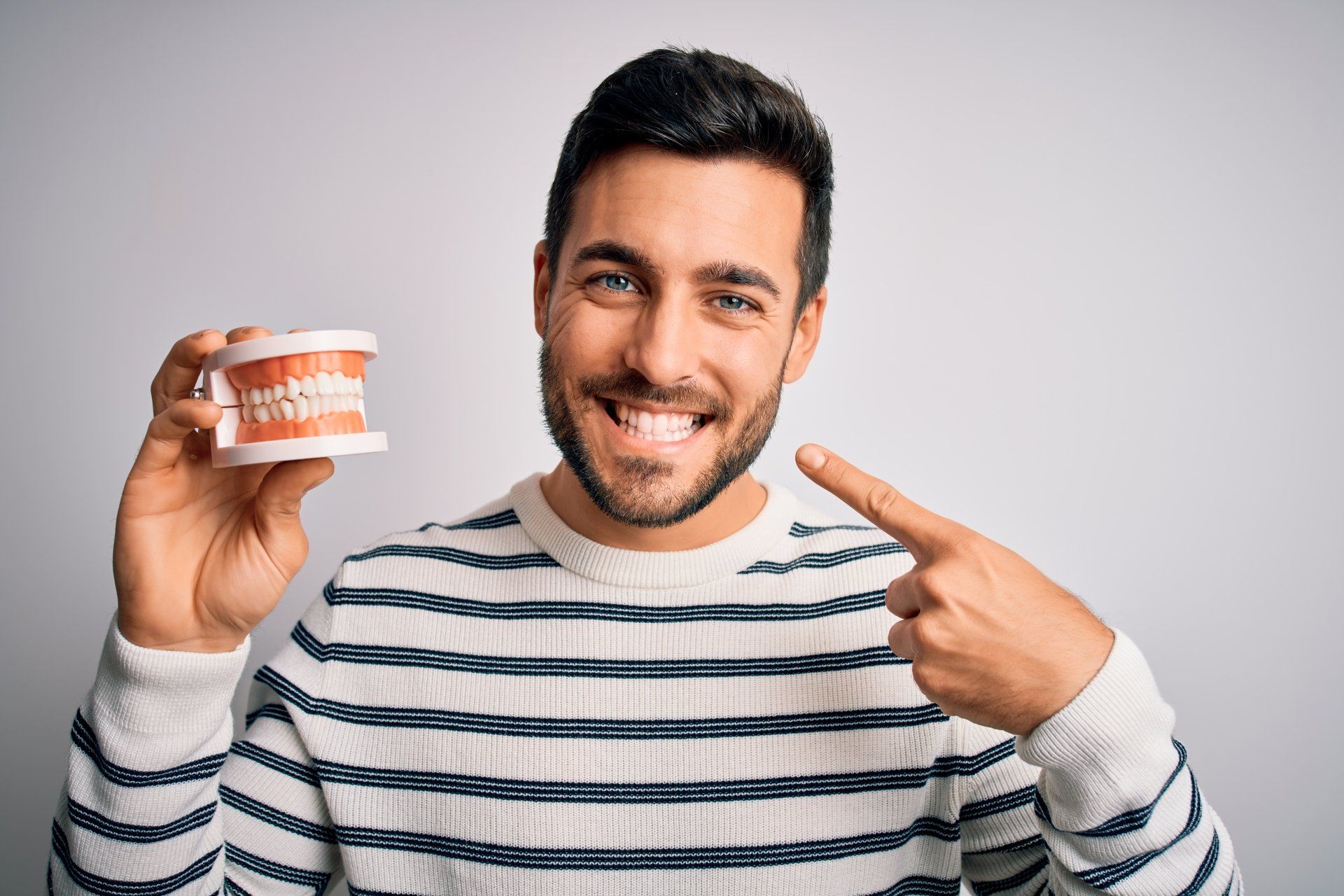 guy smiling a happy smile using one hand to point to his mouth and another to hold a model of upper and lower teeth