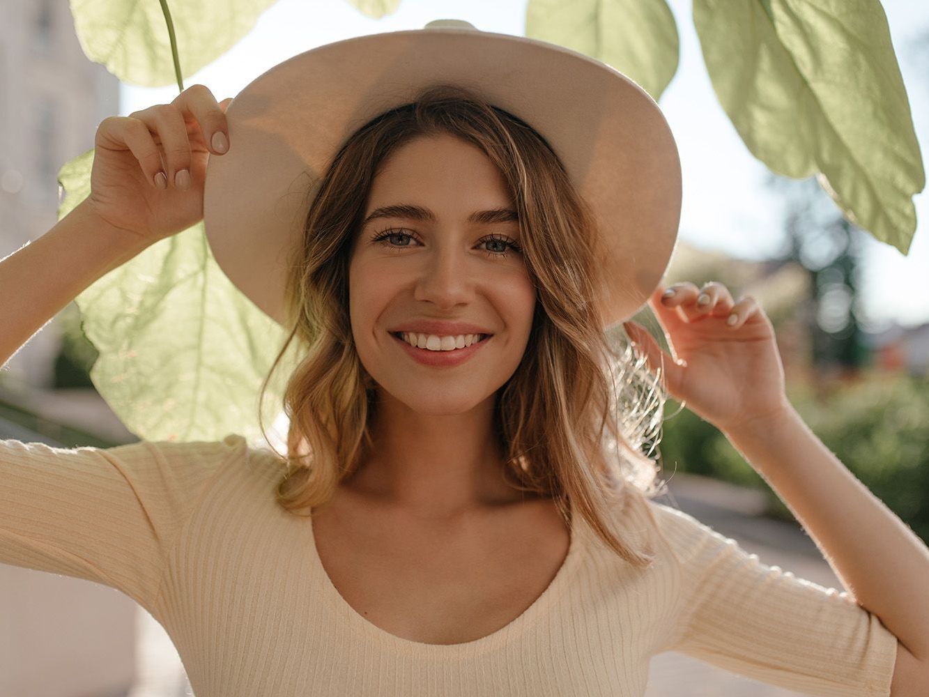 girl standing outside in the sun with a hat on and her arms up happy smiling
