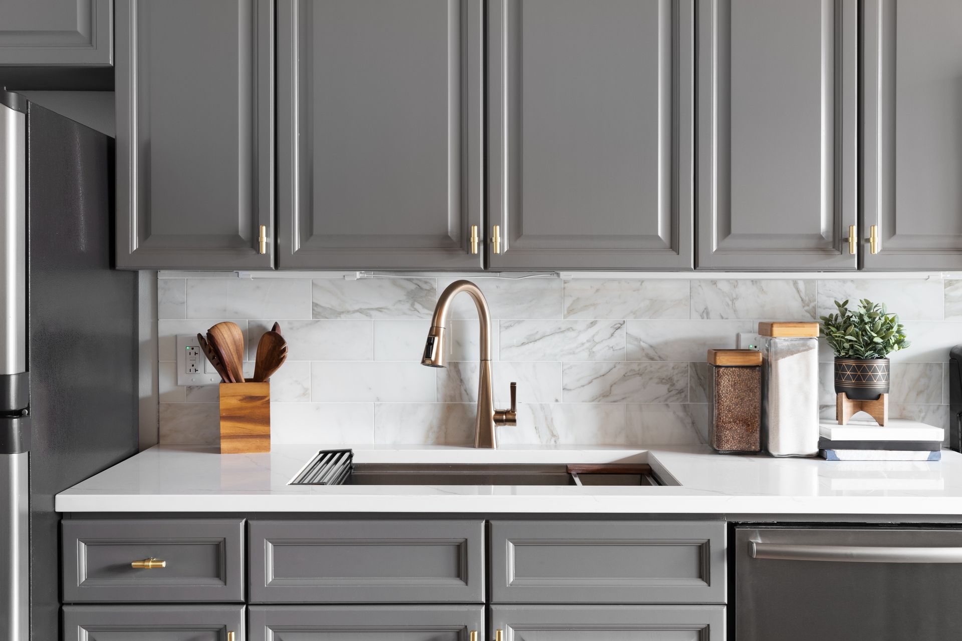 A kitchen sink detail shot with grey cabinets, a white marble countertop, and backsplash. A kitchen sink detail shot with grey cabinets, a white marble countertop, and backsplash.