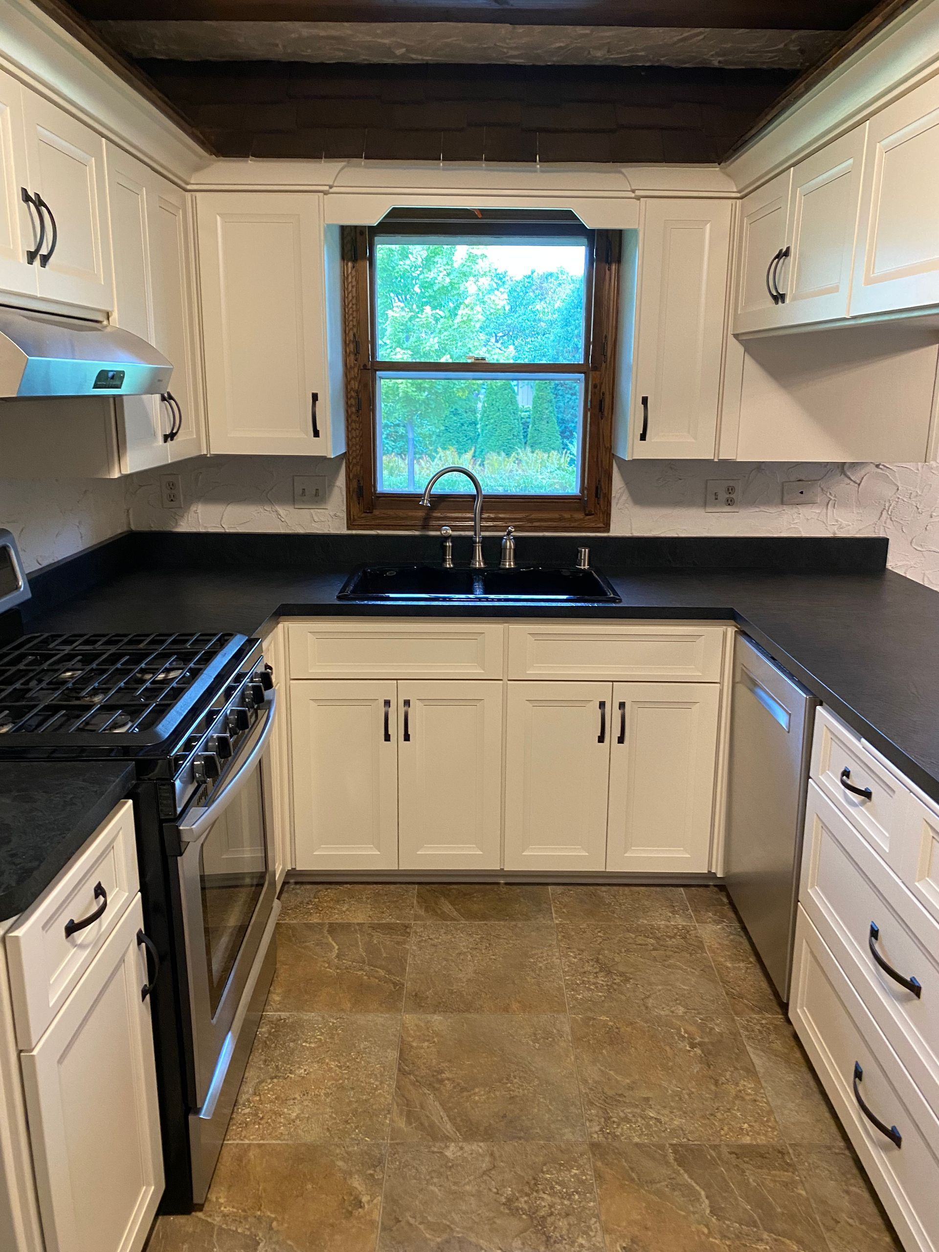 Kitchen with white cabinets, dark countertops, a stainless steel stove, and a window with a view.