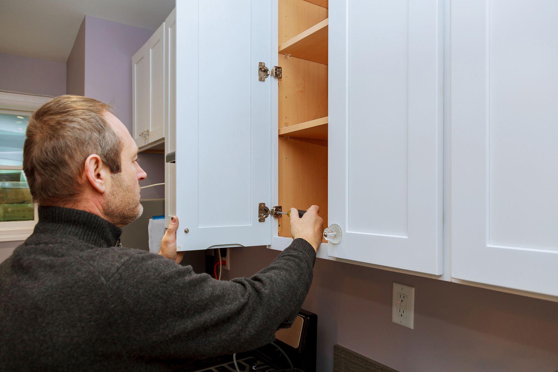 Man inspects kitchen cabinet doors after cabinet resurfacing project in modern home interior.