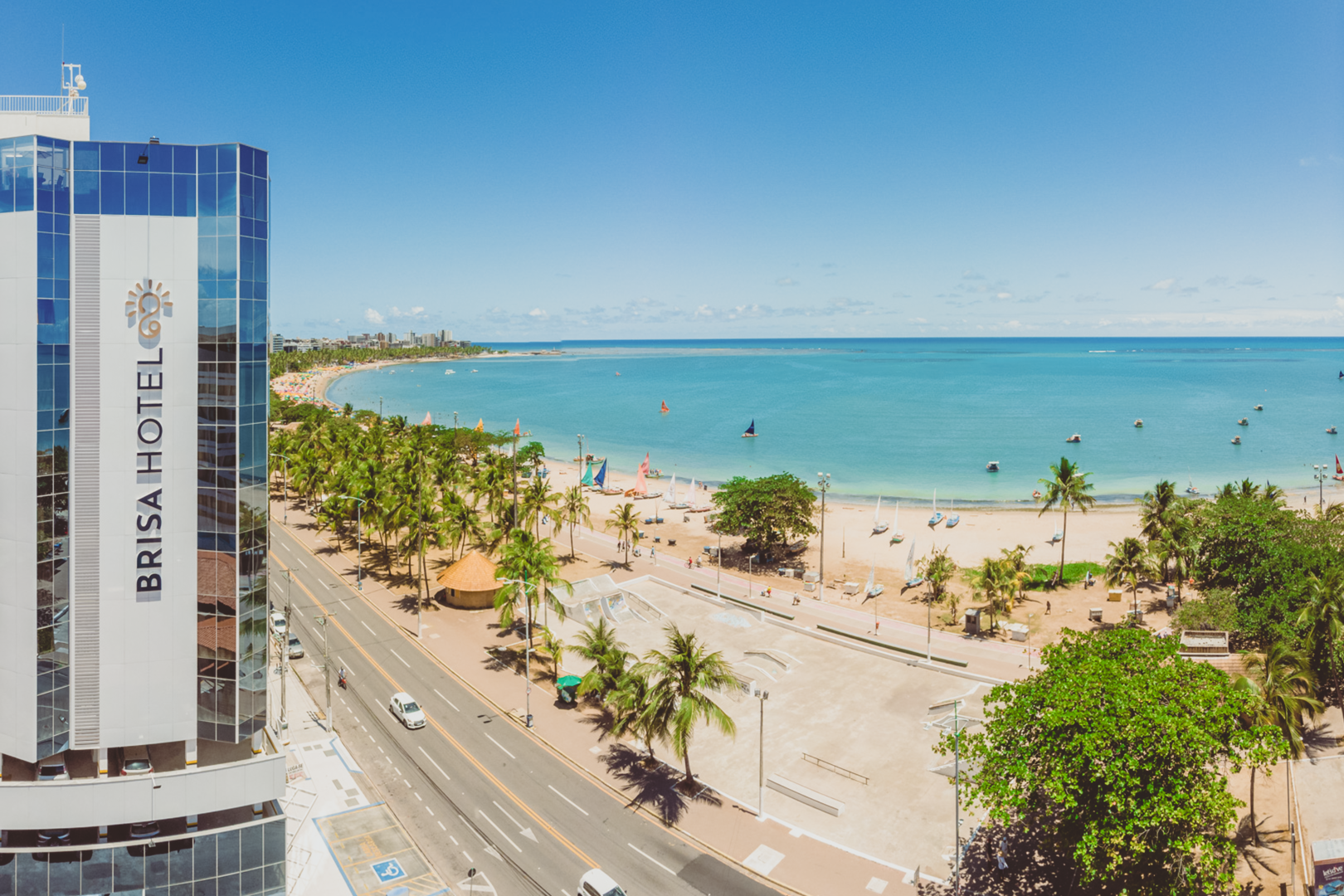 Brisa Hotel com vista para uma praia ensolarada com palmeiras, oceano azul e céu limpo.