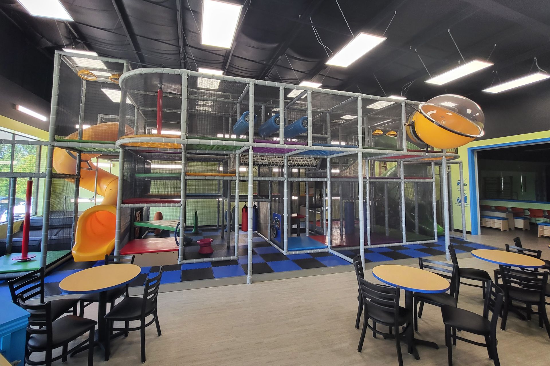 Children in a gymnasium gather around a green mat, with a teacher, interacting and observing.