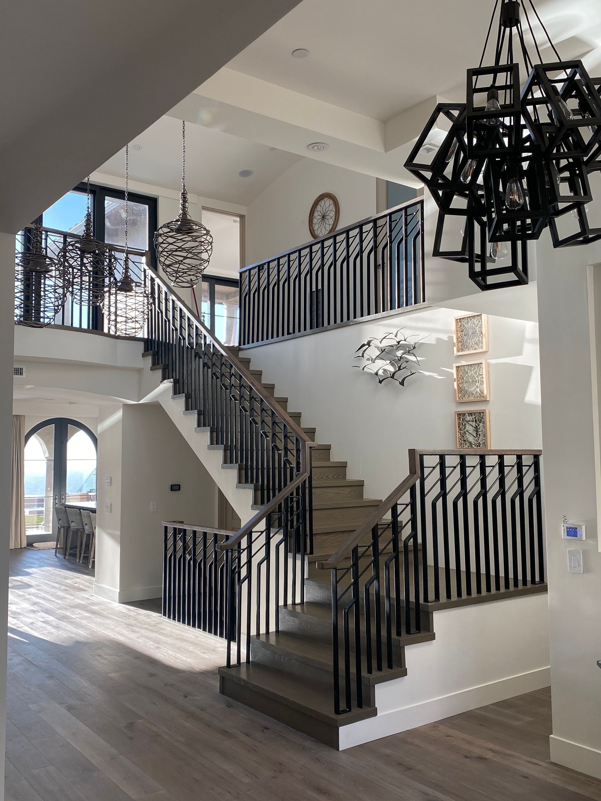 Grand foyer with a staircase, ornate railing, and modern light fixtures.