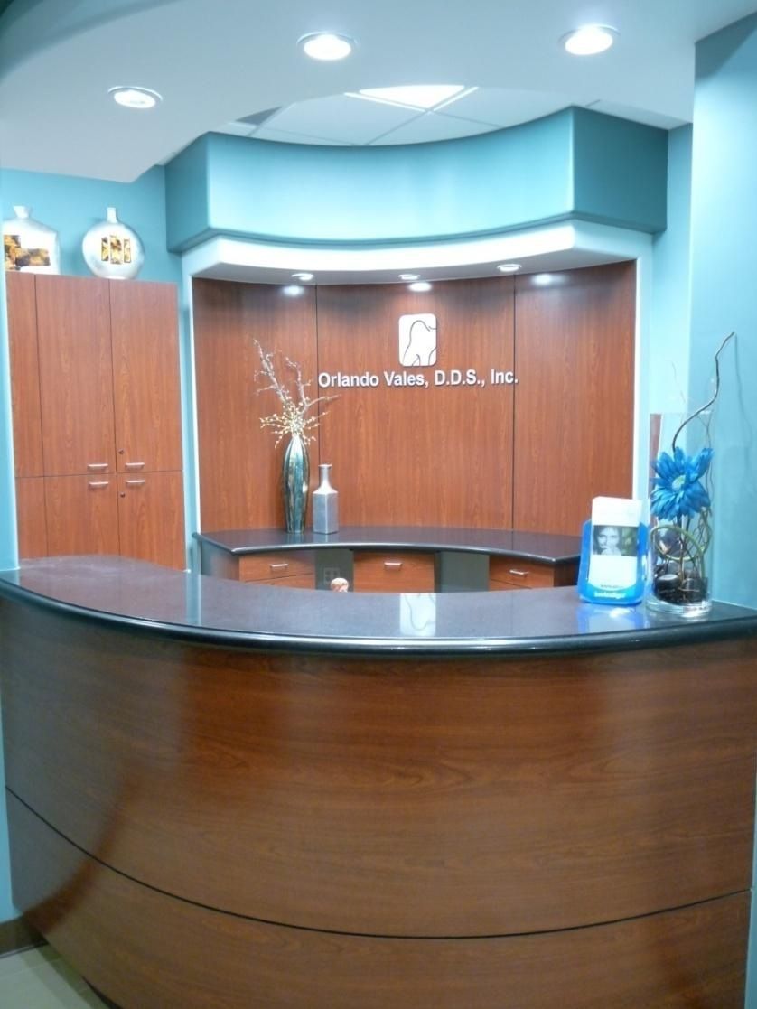 Reception desk in a teal and wood-toned dentist's office with floral arrangements.