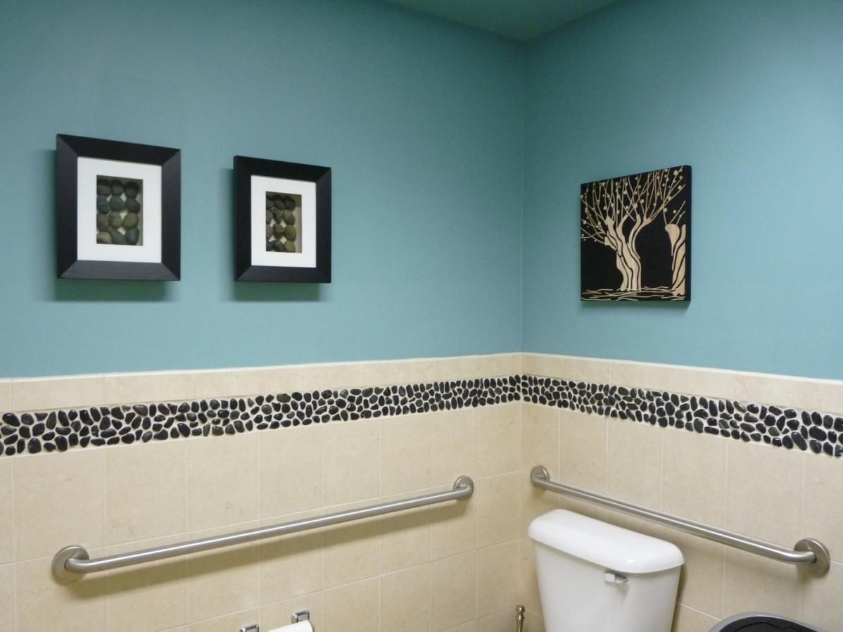Bathroom corner with blue walls, black art, and grab bars. Cream tiles with black stone border.