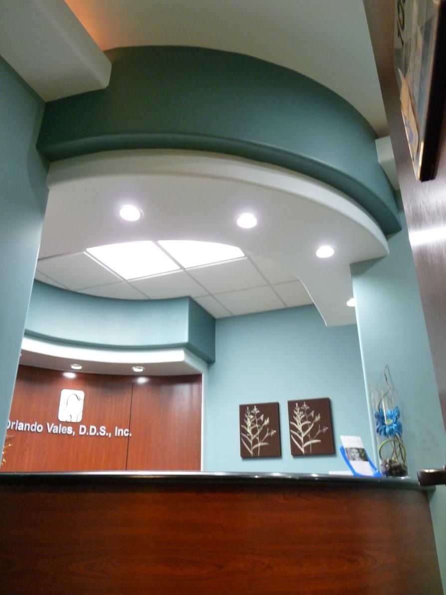 Reception area of a dental office with a curved reception desk, blue and teal walls, and a white ceiling.