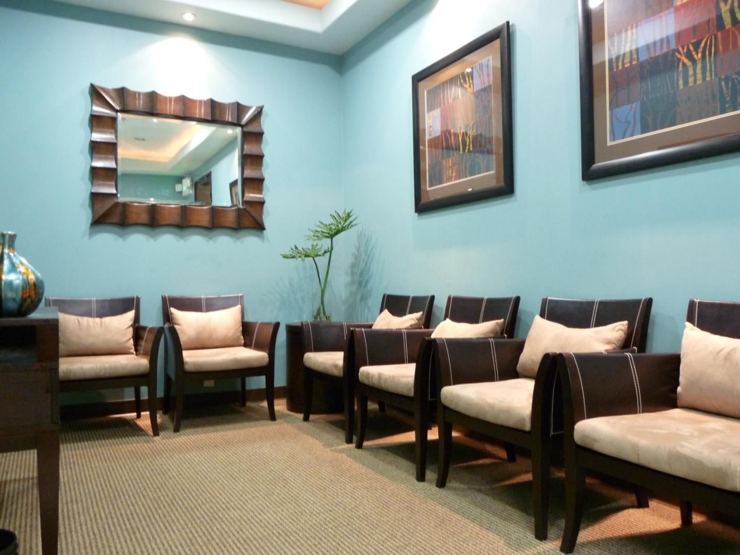 Waiting room with blue walls, wooden chairs, and art.