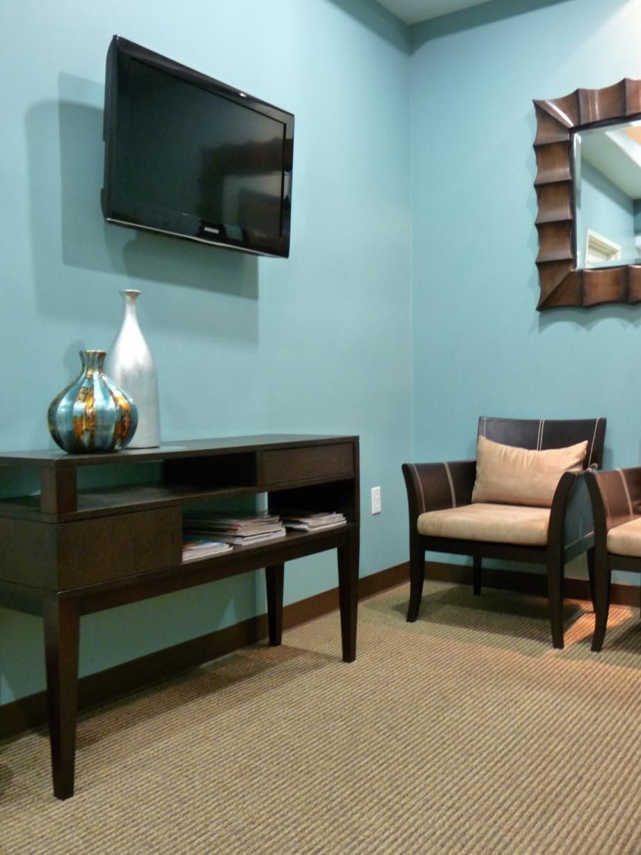 Waiting room with teal walls, brown furniture, TV, mirror, and carpet.